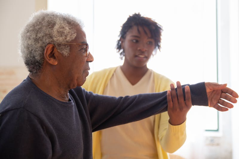 A caregiver helping an elderly man with arm exercises